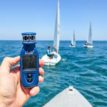 Handheld wind meter with sailboats on the water in the background