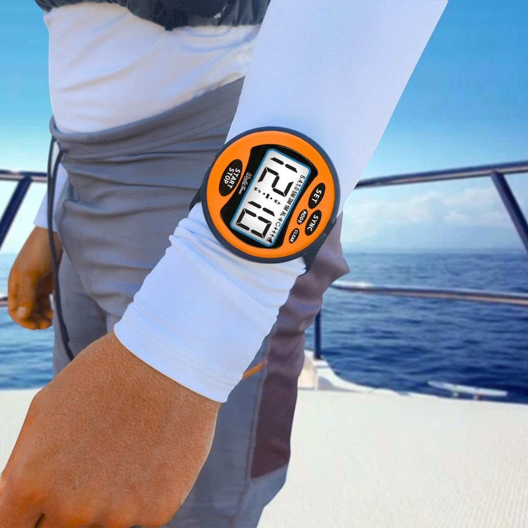 windie.pro orange race stopwatch timer with 5-4-1-0 count, worn on arm over white sleeve, with ocean and boat in background.