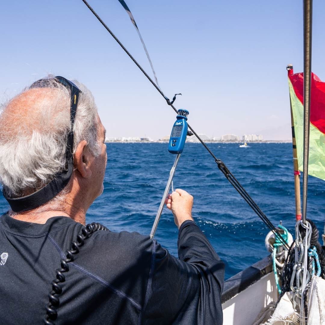 Mark Layer Kit: handheld anemometer with digital display on a sailboat, used by a man for racing.
