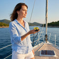 Woman on a sailboat holding a yellow and black anemometer and compass set. Blue sky and water background.