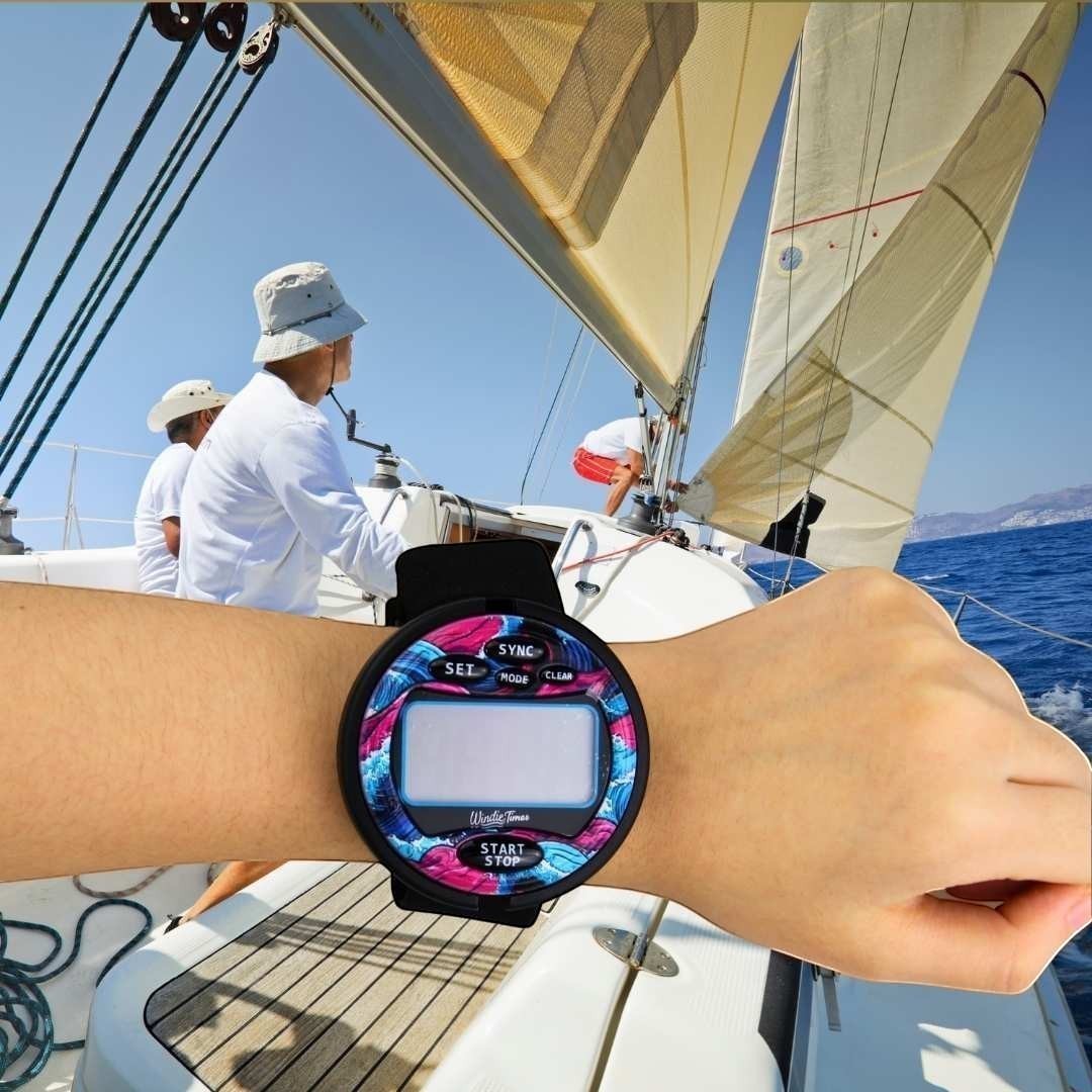Windie.pro sailing timer watch with a pink, blue, and white wave design on the bezel, worn on a wrist while sailing.