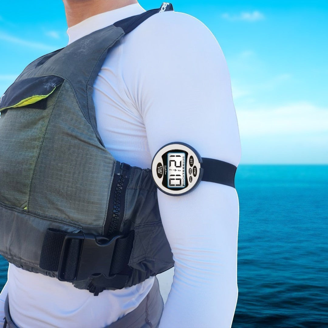 Windie.pro white sailing timer stopwatch worn on arm over white sleeve and grey life vest, against a blue sky and ocean background.